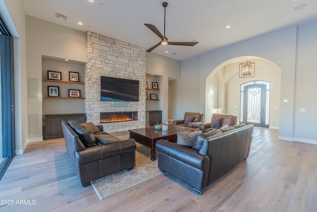 living room with a stone fireplace, ceiling fan, and light wood-type flooring