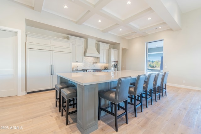 kitchen with a breakfast bar, beamed ceiling, white cabinets, a large island with sink, and custom range hood