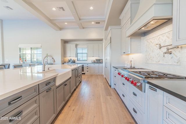 kitchen featuring beamed ceiling, white cabinetry, sink, coffered ceiling, and custom range hood