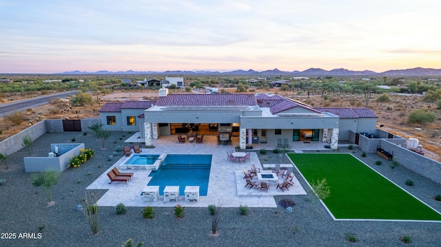 back house at dusk with an in ground hot tub, a mountain view, and a patio area