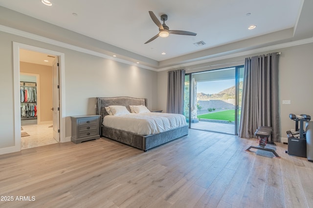 bedroom with ceiling fan, access to exterior, light wood-type flooring, and a tray ceiling