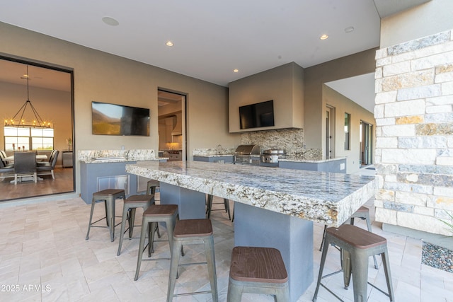 kitchen featuring a breakfast bar, pendant lighting, backsplash, light stone counters, and kitchen peninsula