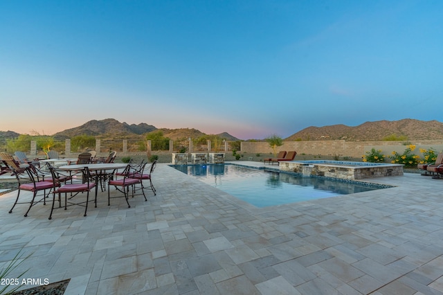 pool at dusk with an in ground hot tub, a mountain view, and a patio