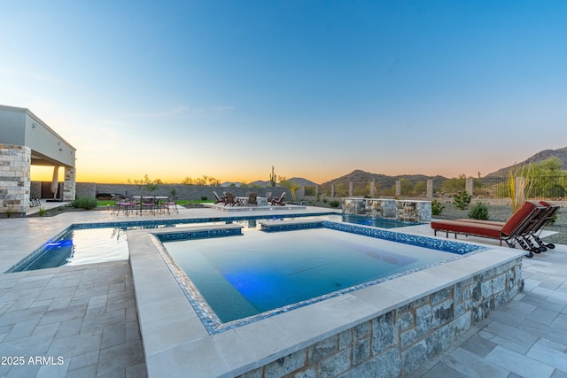 pool at dusk with a jacuzzi, a mountain view, and a patio area