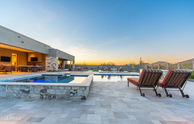 pool at dusk featuring exterior bar, a jacuzzi, and a patio area