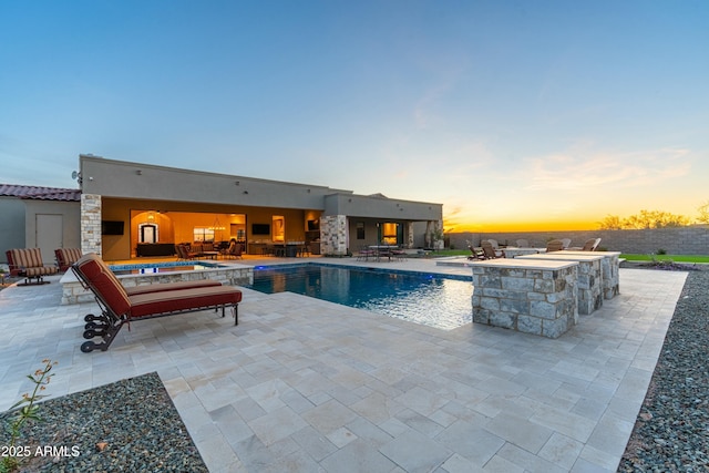 pool at dusk featuring a jacuzzi and a patio area