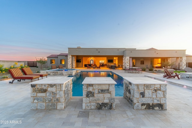 pool at dusk with a patio and an in ground hot tub