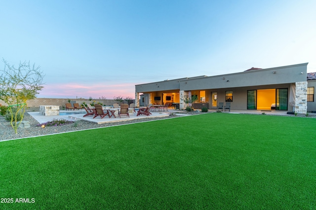 back house at dusk with a lawn and a patio area