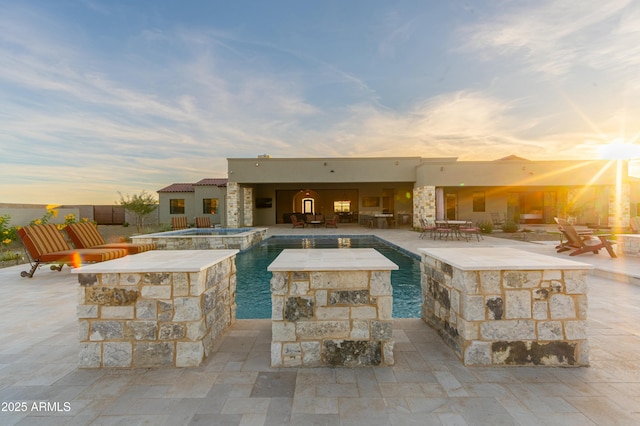 pool at dusk featuring an in ground hot tub and a patio