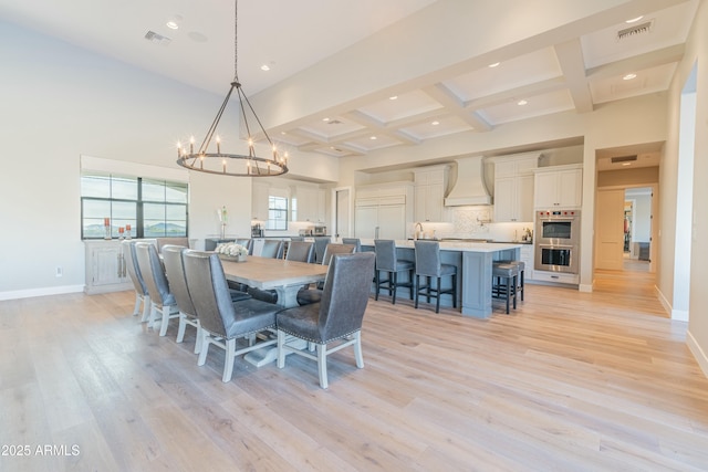 dining area featuring light wood-type flooring, a high ceiling, coffered ceiling, a notable chandelier, and beam ceiling