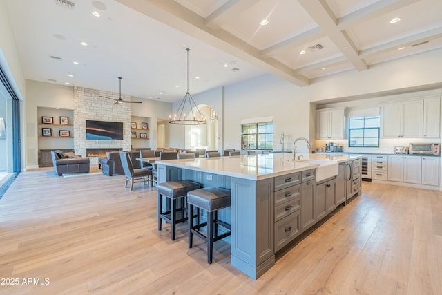 kitchen with a stone fireplace, sink, light wood-type flooring, a large island with sink, and white cabinets