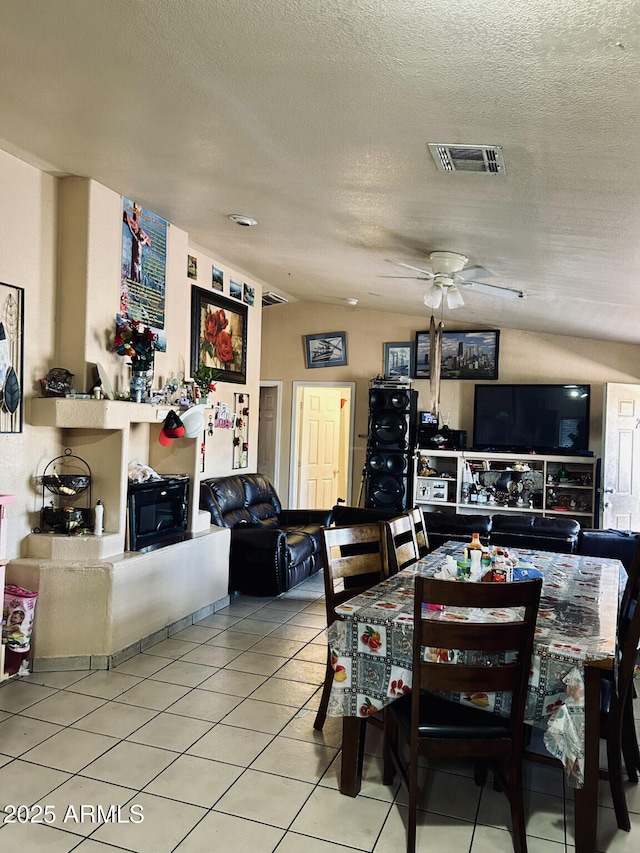 tiled dining space with ceiling fan, vaulted ceiling, and a textured ceiling