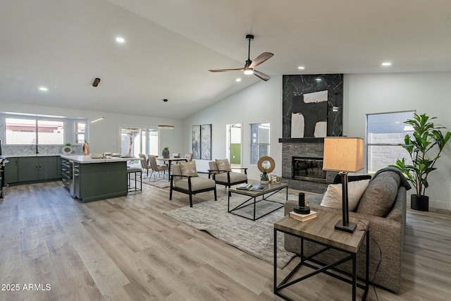 living room featuring a high end fireplace, light wood-type flooring, high vaulted ceiling, and ceiling fan