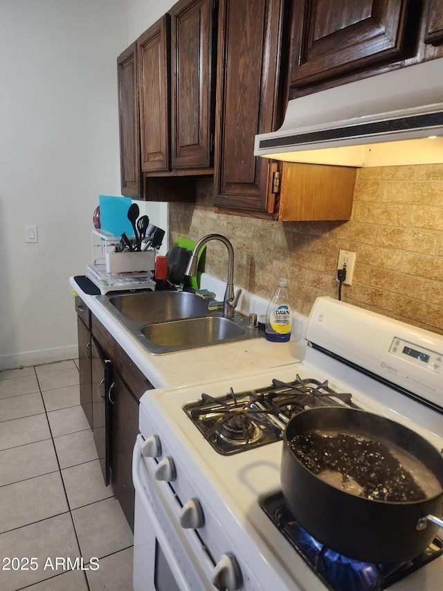 kitchen featuring under cabinet range hood, a sink, light countertops, light tile patterned floors, and white range with gas stovetop