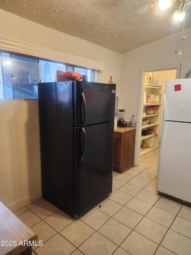 kitchen featuring light tile patterned floors, a textured ceiling, and freestanding refrigerator