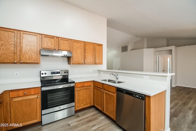 kitchen with a peninsula, stainless steel appliances, light countertops, under cabinet range hood, and a sink