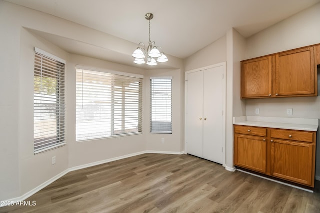 kitchen with brown cabinetry, a chandelier, vaulted ceiling, and light wood finished floors