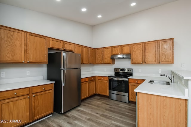 kitchen with brown cabinetry, appliances with stainless steel finishes, wood finished floors, under cabinet range hood, and a sink