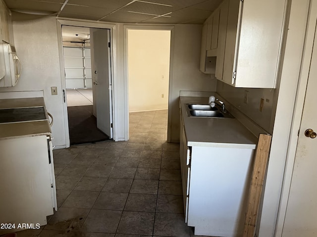 kitchen featuring tile patterned flooring, a paneled ceiling, white cabinetry, and sink