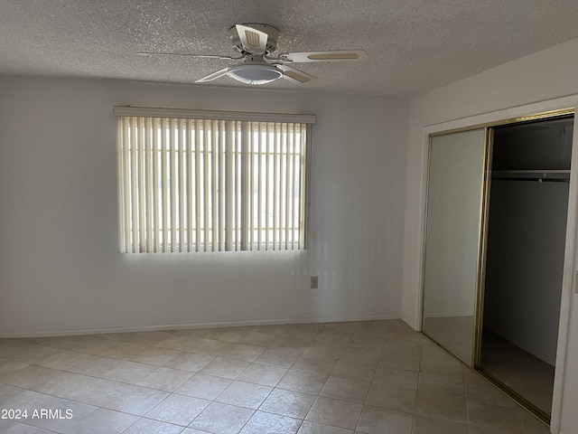 unfurnished bedroom with ceiling fan, a closet, light tile patterned flooring, and a textured ceiling