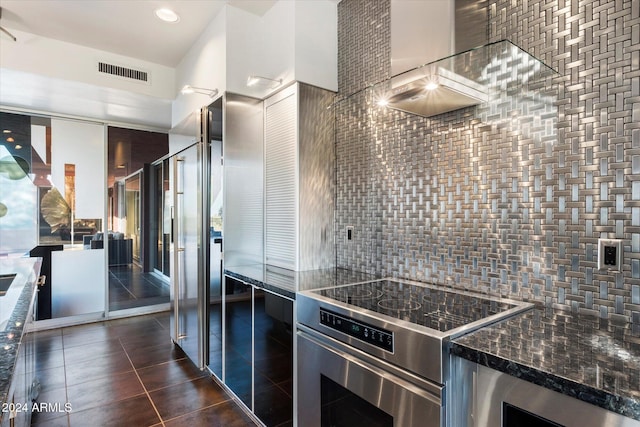 kitchen featuring tasteful backsplash, dark stone countertops, stainless steel range, and dark tile patterned flooring