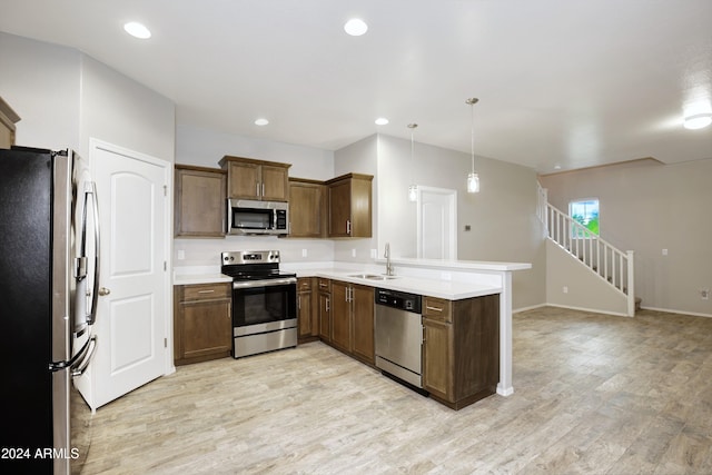 kitchen with stainless steel appliances, sink, kitchen peninsula, decorative light fixtures, and light wood-type flooring