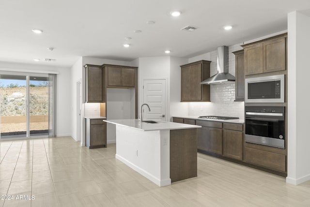 kitchen with sink, wall chimney range hood, tasteful backsplash, a kitchen island with sink, and appliances with stainless steel finishes