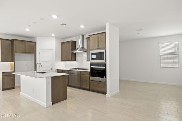 kitchen with a kitchen island with sink, wall chimney range hood, sink, decorative backsplash, and appliances with stainless steel finishes