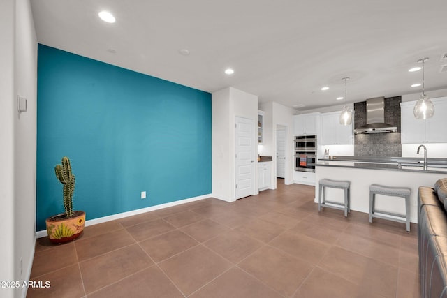 kitchen featuring white cabinetry, a kitchen breakfast bar, double oven, pendant lighting, and wall chimney range hood