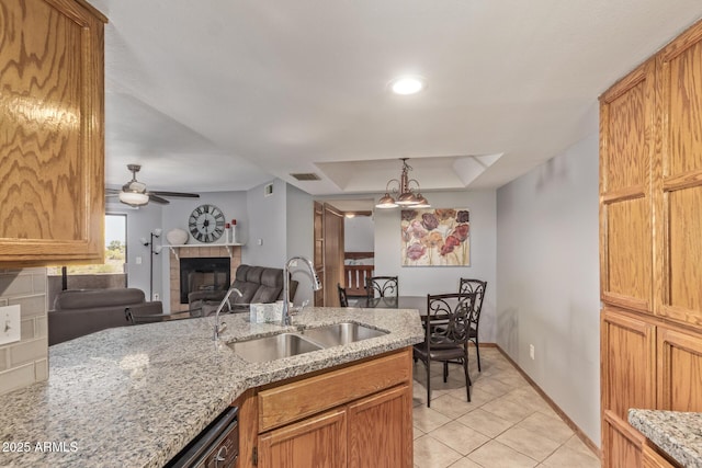 kitchen with a sink, a tray ceiling, a fireplace, light tile patterned floors, and light stone countertops