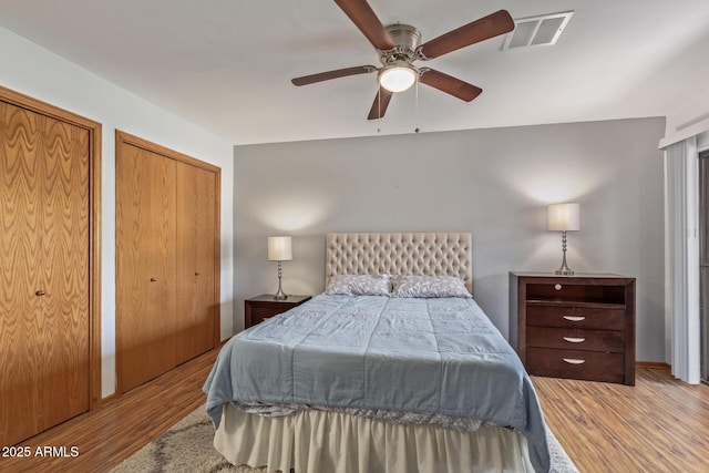 bedroom with two closets, wood finished floors, and a ceiling fan