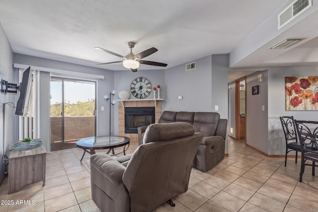 living room featuring light tile patterned floors, ceiling fan, a tiled fireplace, and baseboards