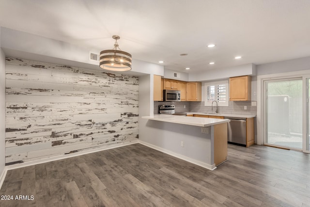 kitchen with appliances with stainless steel finishes, hardwood / wood-style floors, kitchen peninsula, light brown cabinetry, and a breakfast bar