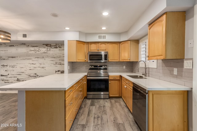 kitchen with appliances with stainless steel finishes, backsplash, light hardwood / wood-style floors, sink, and kitchen peninsula