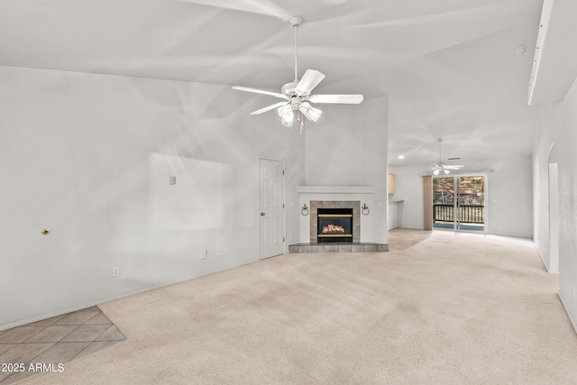 unfurnished living room with ceiling fan, a tiled fireplace, vaulted ceiling, and light carpet