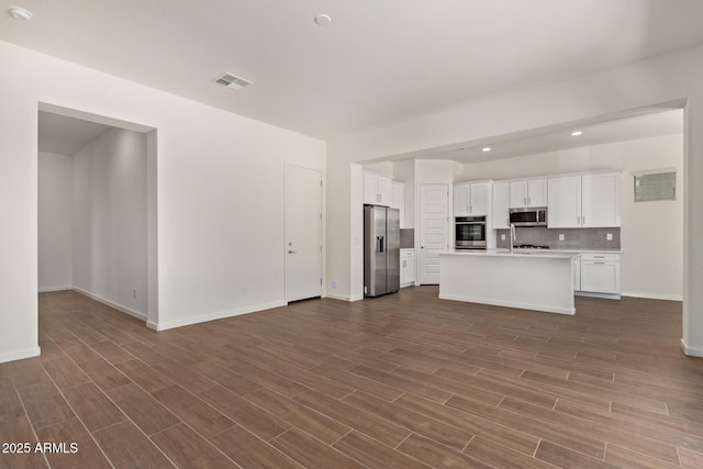 kitchen featuring appliances with stainless steel finishes, open floor plan, light countertops, and an island with sink