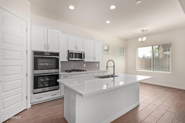 kitchen with a sink, stainless steel appliances, light countertops, and a center island with sink