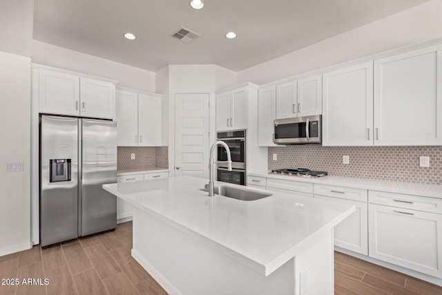 kitchen with visible vents, white cabinets, appliances with stainless steel finishes, a kitchen island with sink, and light countertops