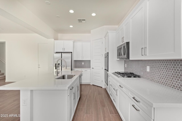 kitchen with stainless steel appliances, white cabinets, light countertops, and a center island with sink