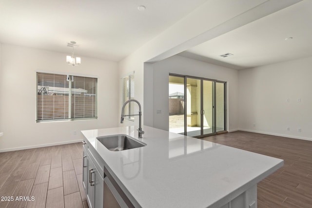 kitchen featuring hanging light fixtures, an inviting chandelier, a kitchen island with sink, a sink, and wood finished floors