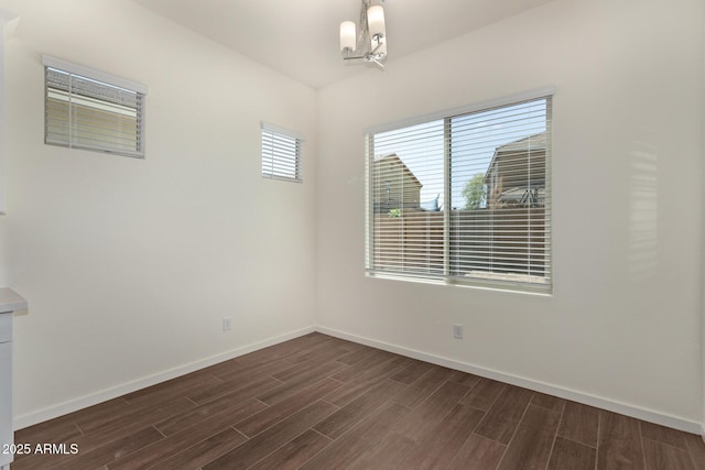 empty room with wood finish floors, a notable chandelier, and baseboards