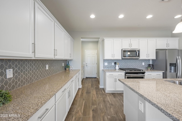 kitchen featuring dark wood-type flooring, stainless steel appliances, light stone countertops, white cabinets, and decorative backsplash