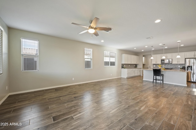 unfurnished living room featuring plenty of natural light, dark hardwood / wood-style floors, and ceiling fan