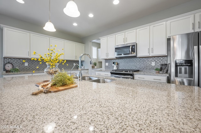 kitchen featuring sink, appliances with stainless steel finishes, white cabinetry, hanging light fixtures, and light stone counters