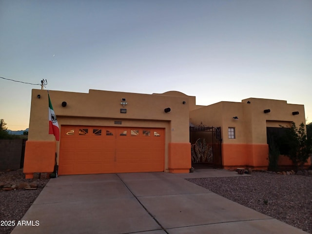 pueblo-style house with driveway, an attached garage, a gate, and stucco siding