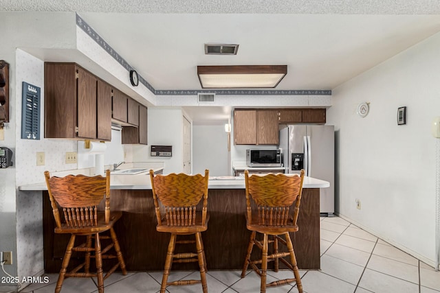 kitchen featuring light tile patterned floors, a breakfast bar, kitchen peninsula, and appliances with stainless steel finishes