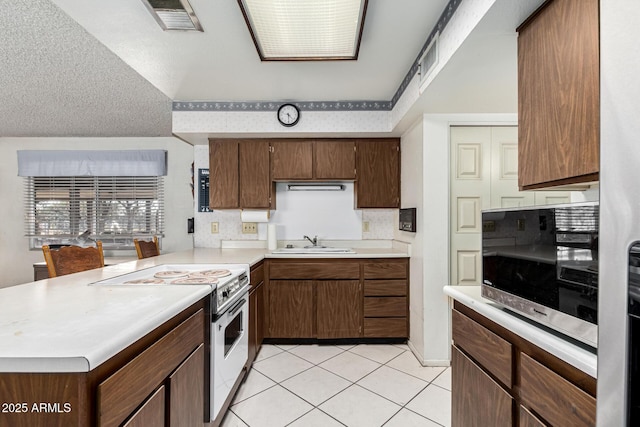 kitchen with white electric range, sink, a textured ceiling, light tile patterned floors, and kitchen peninsula