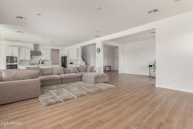 living area with stairway, light wood-style floors, and visible vents