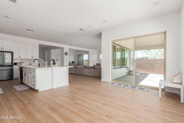 kitchen with visible vents, white cabinets, light wood-type flooring, and decorative backsplash