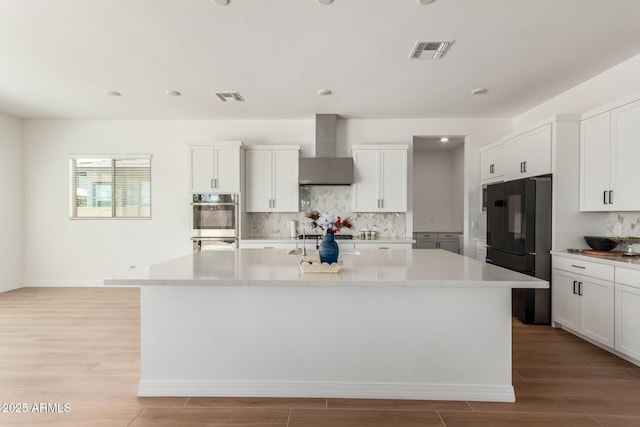 kitchen with visible vents, light wood-style floors, wall chimney exhaust hood, and light countertops